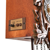 Close-up of the Pitched Roof Quartz Wooden Cuckoo Wall Clock in mahogany, showing the side control panel with volume dial and reset/adjust buttons beside the carved wood case and Roman numeral dial.