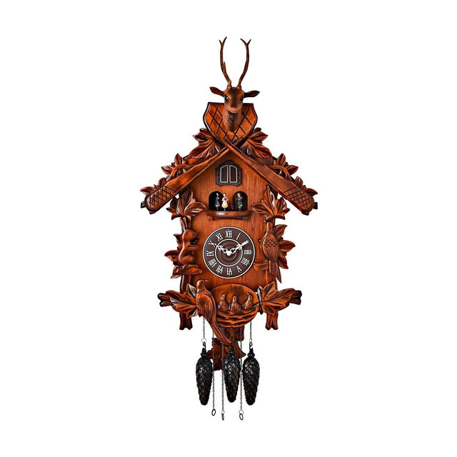 Mahogany wooden cuckoo wall clock with a carved stag's head and antlers atop a pitched roof, roundabout figures, a bird, and hanging pinecone weights, shown on a white background.