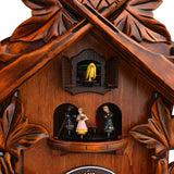 Close-up of the Stag Wooden Quartz Cuckoo Wall Clock in mahogany, showing carved leaf gables, a shuttered bird door with yellow cuckoo, and three painted figures on a roundabout.