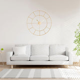 Gold double ring skeleton wall clock, 80cm, with spade hands and hour bars, hung above a light grey sofa in a living room.