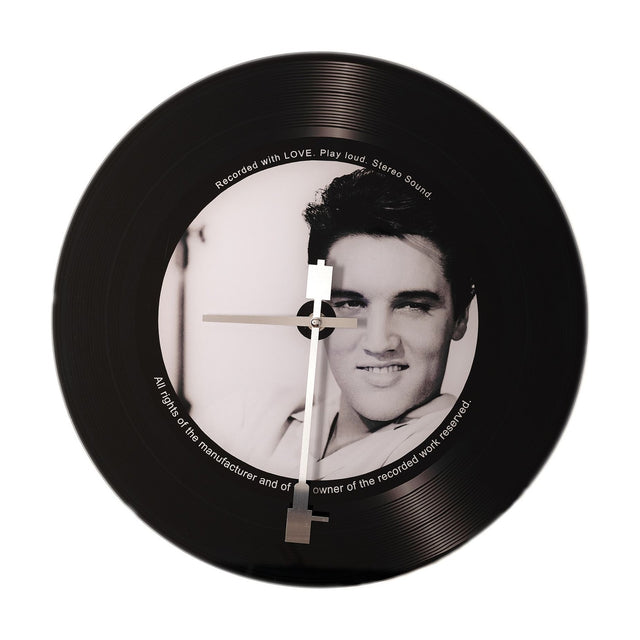 Round black glass wall clock styled as a vinyl record with grooved rim, silver needle hands, and a black-and-white portrait label with printed text, on a plain white background.