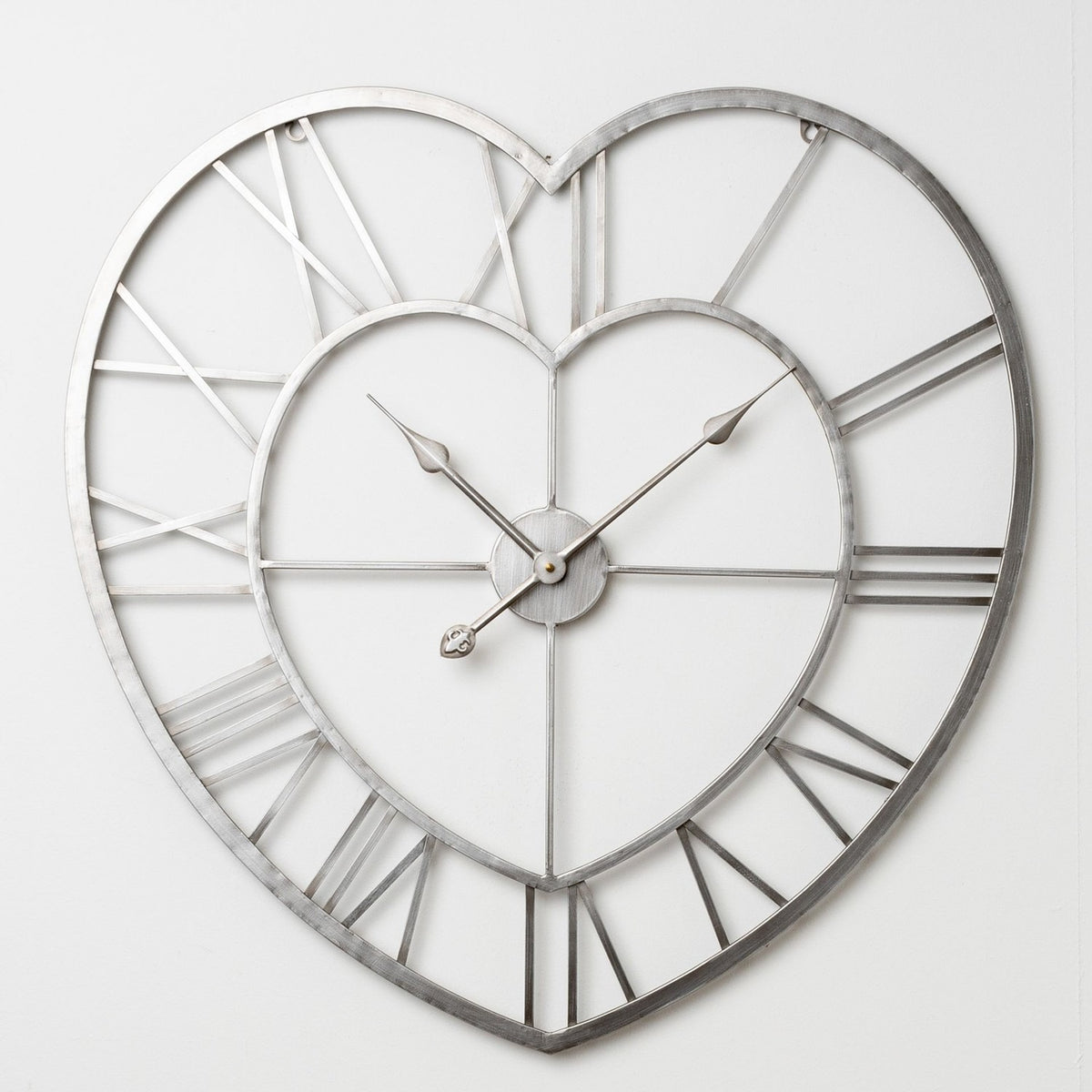Open Heart Metal Wall Clock in silver finish with cut-out Roman numerals between double heart outlines and slim hands, shown on a plain white background.