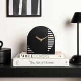 Black arched steel mantel clock with gold hands and cut-out horizontal stripe detailing, displayed on stacked books on a dark shelf.