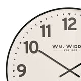 Close-up of a round metal wall clock with a white dial, bold black Arabic numerals, black hands, and a slim black rim.