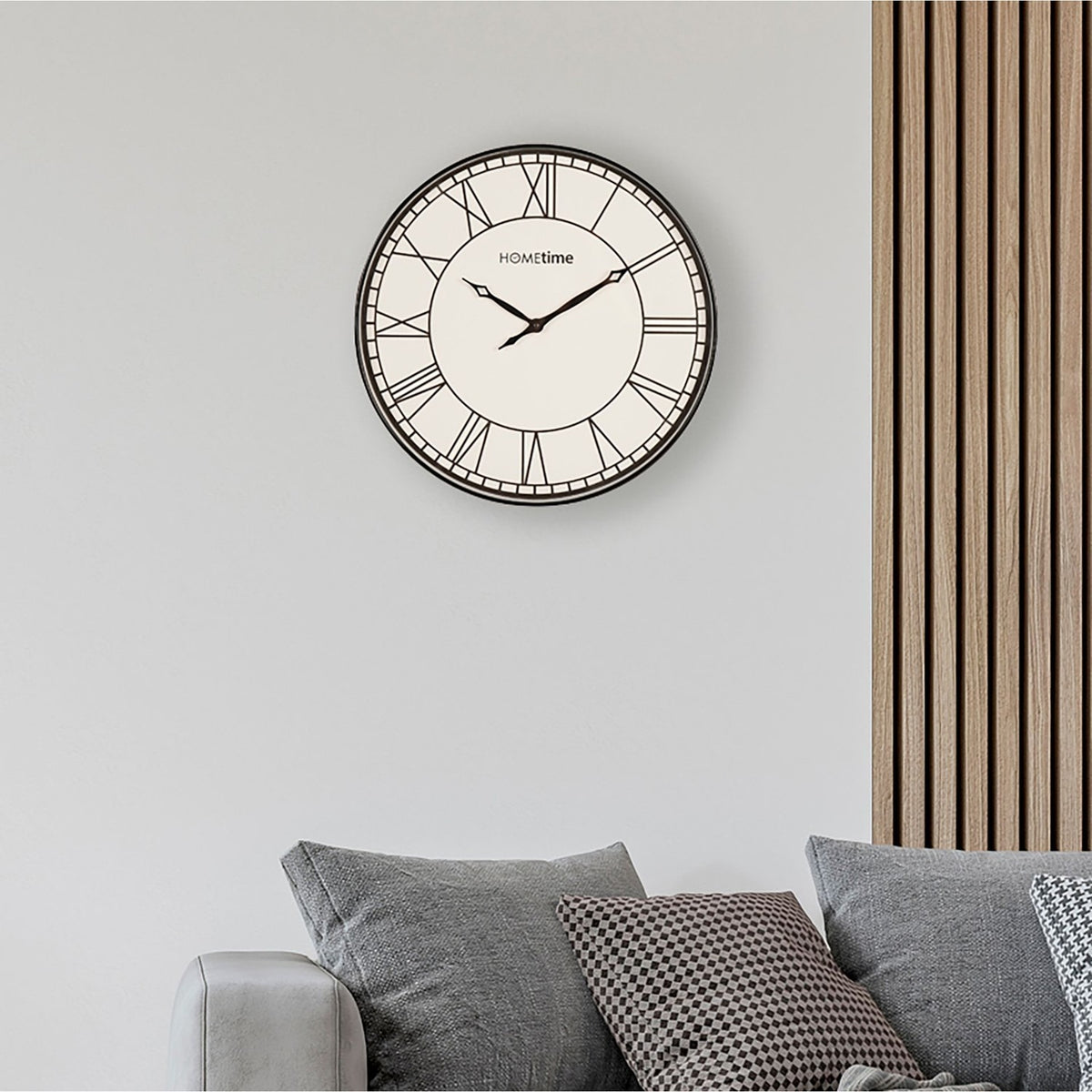 Round Roman Dial Quartz Wall Clock, 50.5cm, with black case and white face, mounted on a grey living room wall above a grey sofa with cushions.