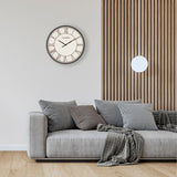 Round Roman Dial Quartz Wall Clock 50.5cm in black and white, displayed on a light grey wall above a grey sofa with patterned cushions in a living room setting.