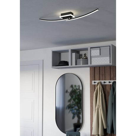 Warvanne LED Flush Ceiling Light in black, two curved illuminated arms from a square base, shown mounted above a hallway mirror and cabinet.