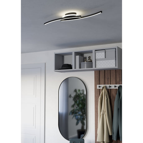 Warvanne LED flush ceiling light in black with two curved steel arms crossing over a round canopy, illuminated on a hallway ceiling above a wall mirror and coat hooks.