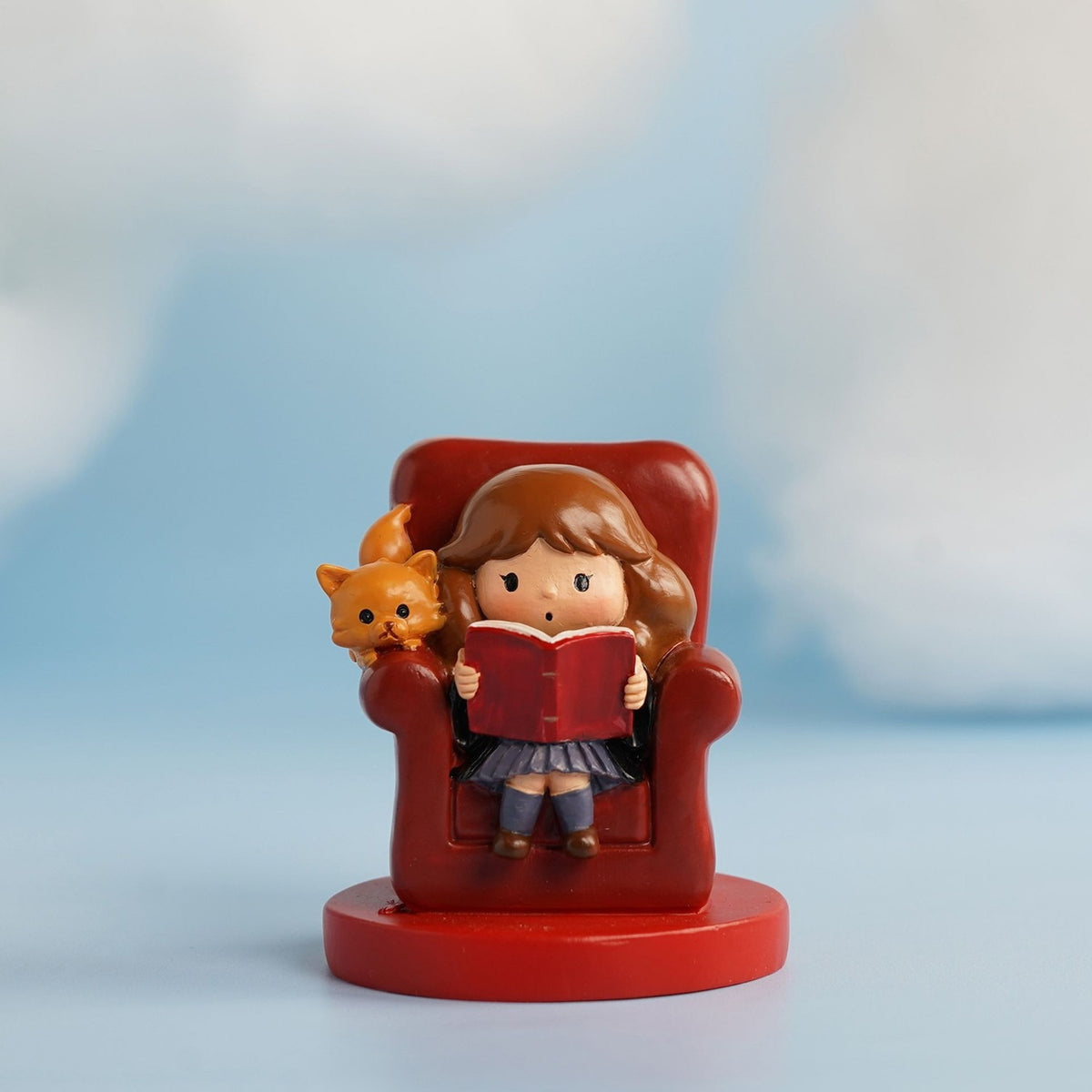 Harry Potter Hermione and Crookshanks resin figurine in red, seated in an armchair reading a book with her ginger cat beside her, on a round red base.