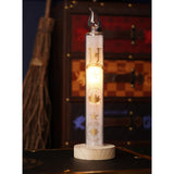 Harry Potter Hogwarts Yule Ball glass LED candle, 29.5cm white column with clear flame tip and gold Hogwarts crest, castle and starburst print, on a wooden base in a living room setting.