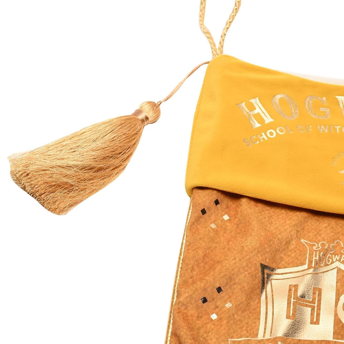 Harry Potter Hufflepuff Christmas stocking in yellow and gold, close-up of the gold tassel hanger and "HOGWARTS" lettered cuff above the house crest on the body, shown on a white background.
