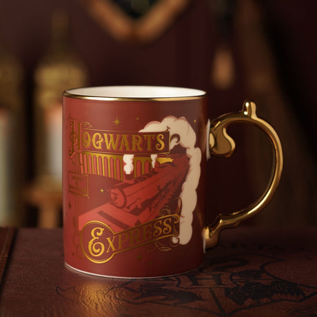 Harry Potter Hogwarts Express porcelain mug in matt burgundy with gold handle, showing the train, arches and gold lettering, set against a blurred dark backdrop.