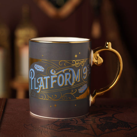 Harry Potter Platform 9¾ porcelain mug in dark blue with gold rim, handle, and scrolled banner design, shown on a dark surface with a blurred background.