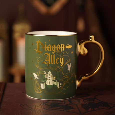 Green porcelain Diagon Alley mug with gold handle, featuring gold Gothic lettering, scrollwork, shopfronts, a domed building, and owl motifs.
