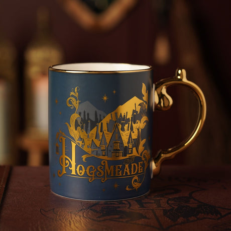 Harry Potter Hogsmeade Collectable Mug in dark blue matt porcelain with a gold handle and gold-lettered Hogsmeade village scene featuring rooftops, mountains, stars and a lantern.