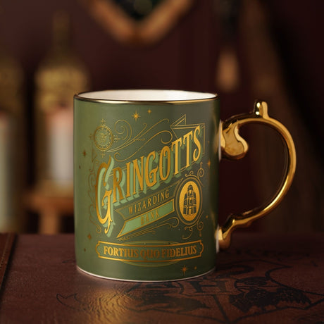 Green and gold porcelain mug with gold handle, featuring "Gringotts Wizarding Bank" lettering, motto "Fortius Quo Fidelius," and an oval bank building emblem.