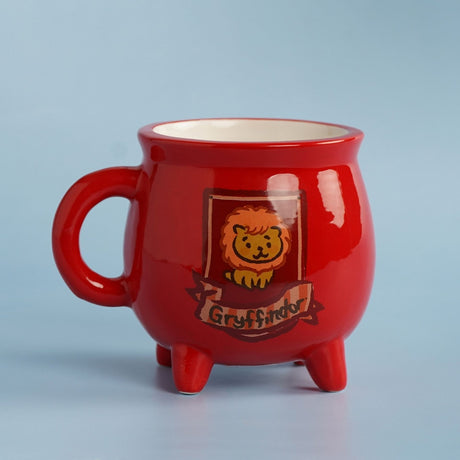 Harry Potter Gryffindor Cauldron Stoneware Mug, red glossy ceramic with three short feet, lion and banner design on a light blue background.