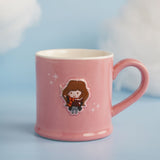 Pink stoneware mug with an embossed cartoon Hermione Granger design holding a wand and book, white interior, pink handle, set against a soft blue background.