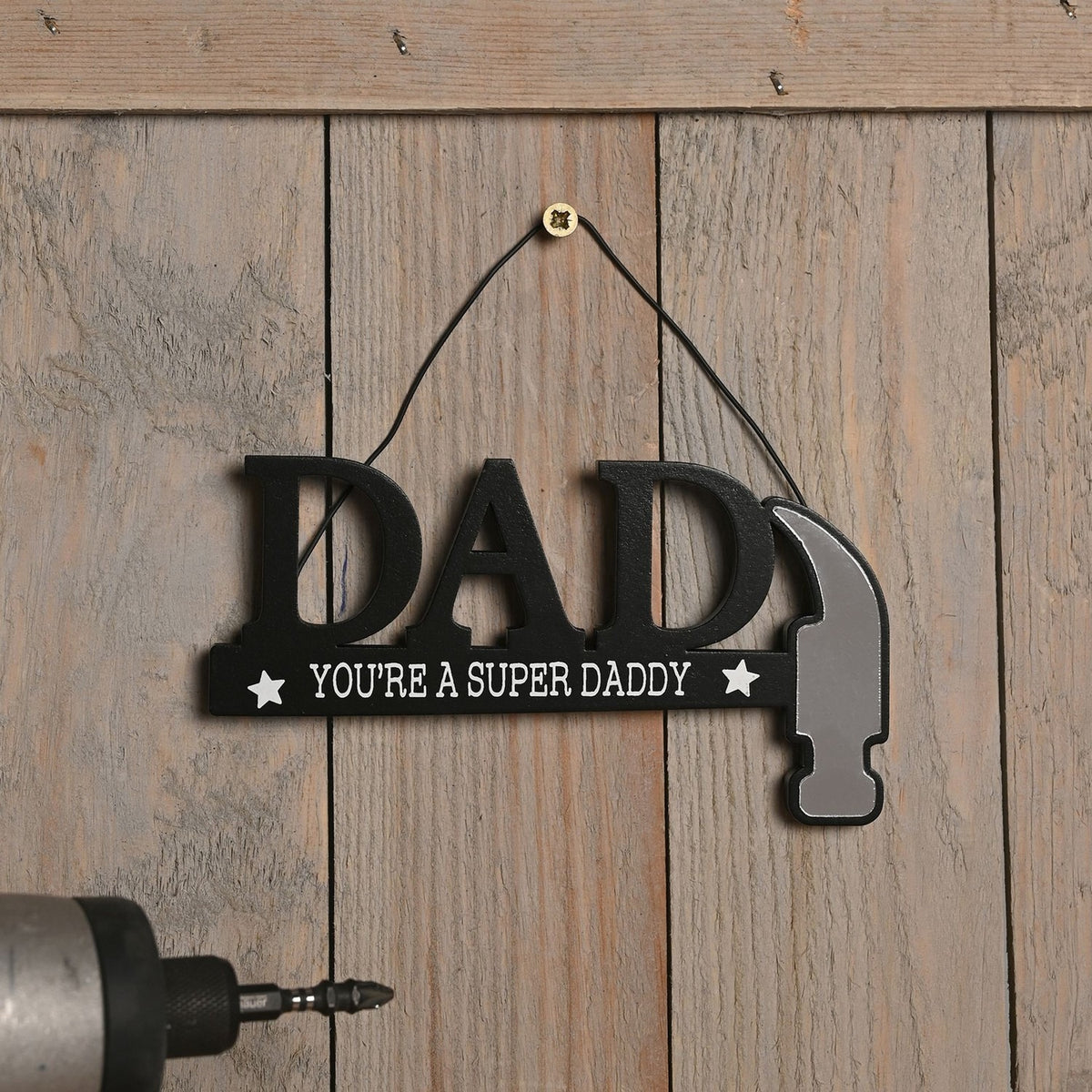 Wooden DAD wall plaque in black with "You're A Super Daddy" text and white stars, the last letter shaped as a hammer with silver head, hung on a wooden panel.