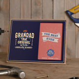 Wooden landscape photo frame, 6x4in, with navy blue front reading "Grandad True Original, Absolute Classic", crown detail, beside a pink "The Best Ever" photo insert, shown on a workbench with tools.