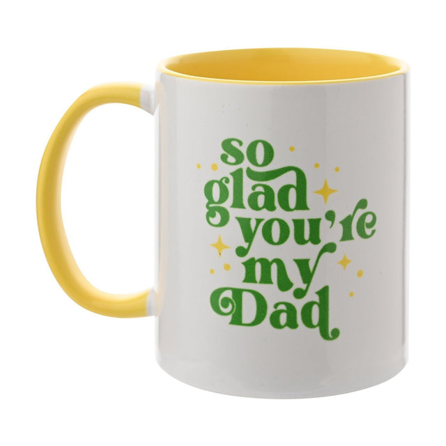 White stoneware mug with yellow handle and interior, featuring "So Glad You're My Dad" in green curled lettering with yellow stars, on a plain background.