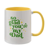White stoneware mug with yellow interior and handle, "so glad you're my Dad" in green lettering with yellow stars, on a plain white background.