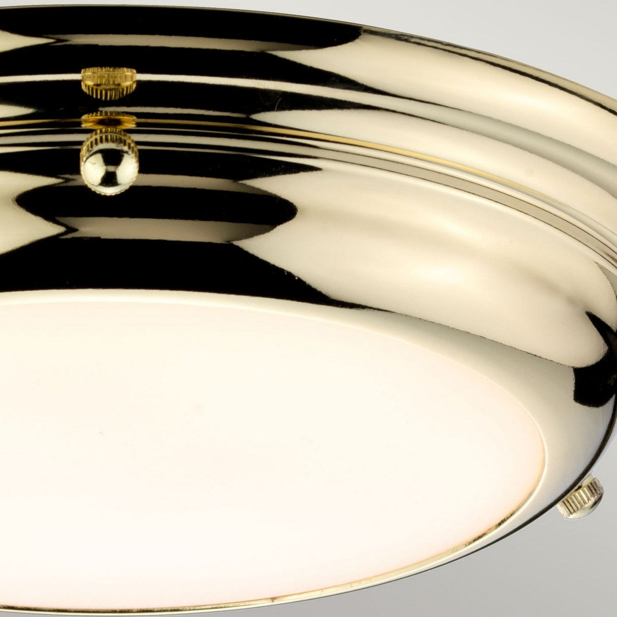 A close-up of the Welland LED Light Mini Flush in polished brass, showcasing its stylish appeal with a white glass cover. The reflective surface includes two small screws, and when turned on, it emits a warm glow. Its reliable performance is highlighted by an IP54 rating.