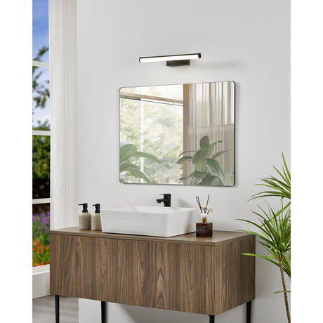 Wenelle LED Bathroom Wall Light 40cm in black, a slim bar fixture mounted above a square mirror over a wood vanity with white countertop basin in a bright bathroom.