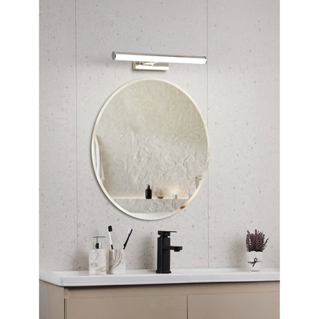 Wenelle LED bathroom wall light in chrome, a slim rounded bar fixture mounted above a round mirror in a bathroom with a white countertop and black tap.