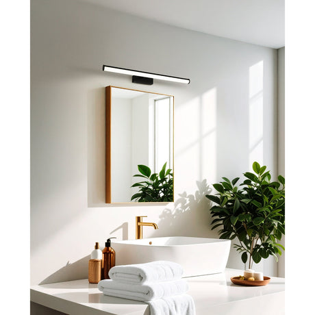 Wenelle 60cm LED bathroom wall light in black, slim bar fixture mounted above a gold-framed mirror in a white bathroom with a vessel sink and plants.