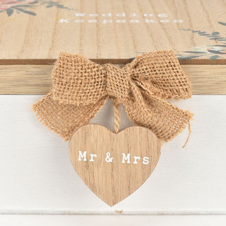 Close-up of a square wooden Wedding Keepsakes box with floral corner print, white base, and a burlap bow holding a wooden "Mr & Mrs" heart tag.