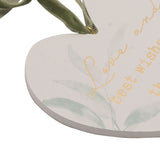 Close-up of the white heart-shaped hanging plaque with sage green foliage and gold script reading "Love and best wishes," suspended by a sage velvet ribbon.