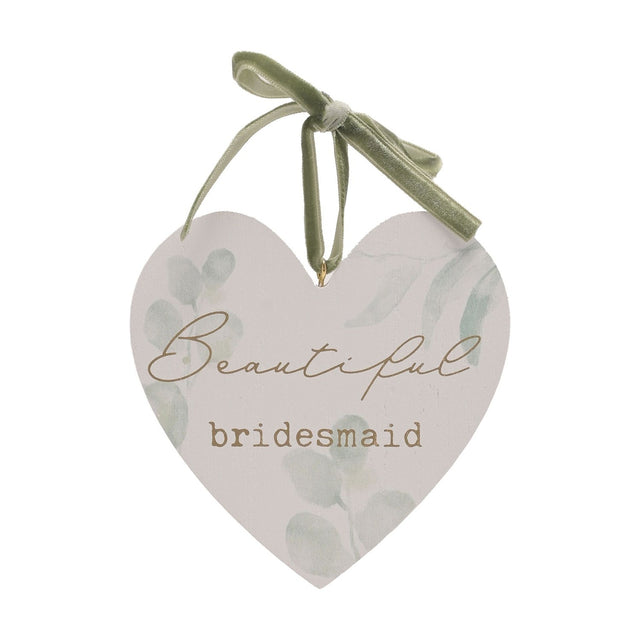 White wooden heart-shaped hanging plaque with pale green leaf print, "Beautiful bridesmaid" in gold script and typewriter lettering, hung by a sage green ribbon bow, on a plain white background.