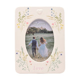 White ceramic photo frame with oval window for a 6 x 4in photo, pastel wildflower sprays at each corner, a raised heart detail, and "Love" printed below in pink.
