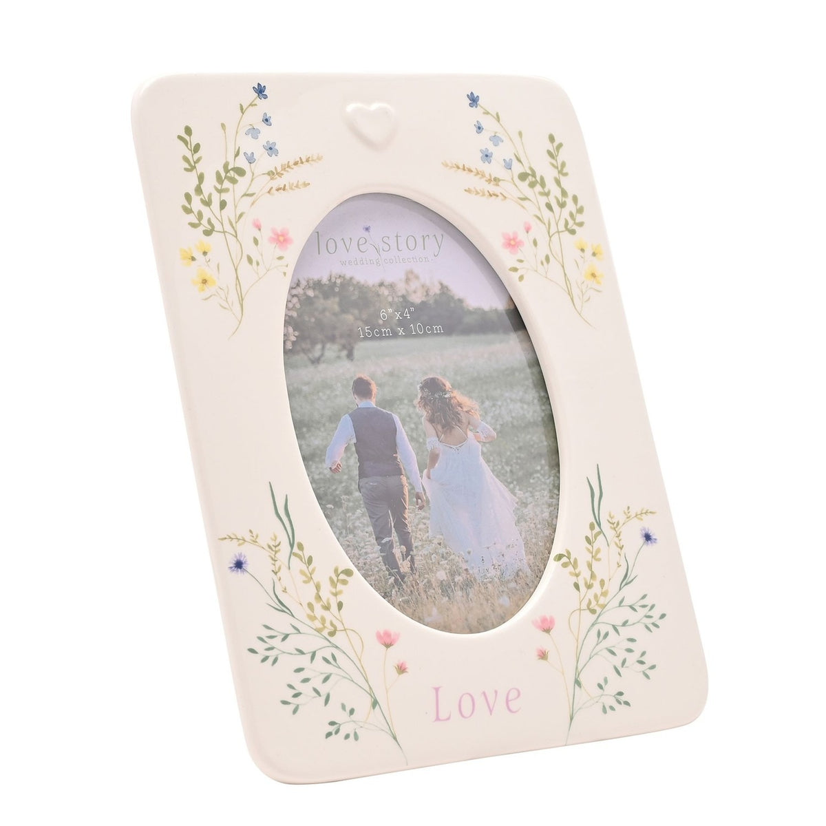 White ceramic photo frame with oval window, pastel wildflower sprays at each corner, raised heart detail, and "Love" printed below, holding a 6 x 4in photo on a plain background.