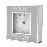 Square mantel clock, 15cm, with mirrored grey border and white dial, inscribed "Love begins in a moment, grows over time and lasts for eternity," on a plain white background.