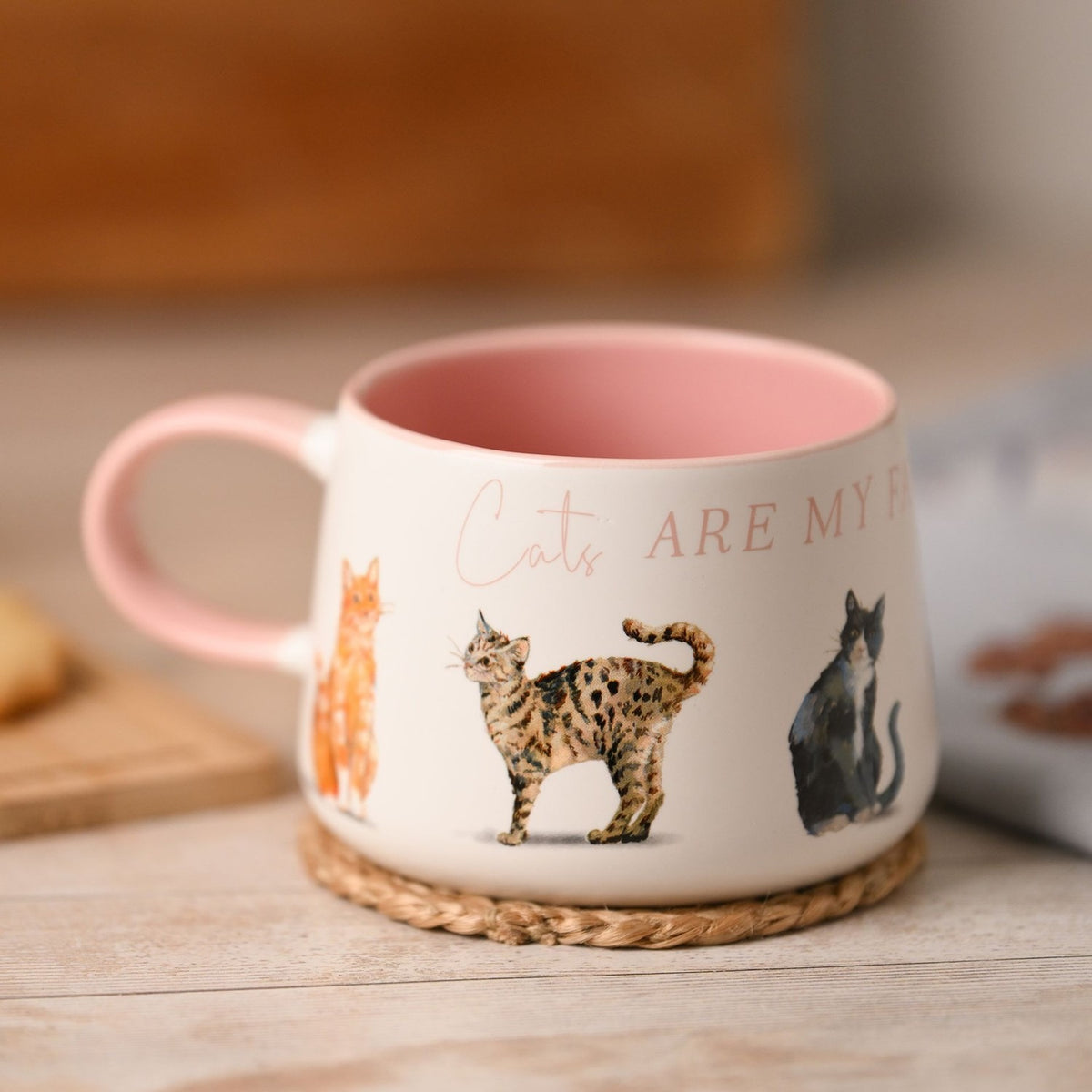 White ceramic mug with pink handle and interior, featuring "Cats Are My Favourite People" text and watercolour-style cat illustrations, shown on a woven coaster.