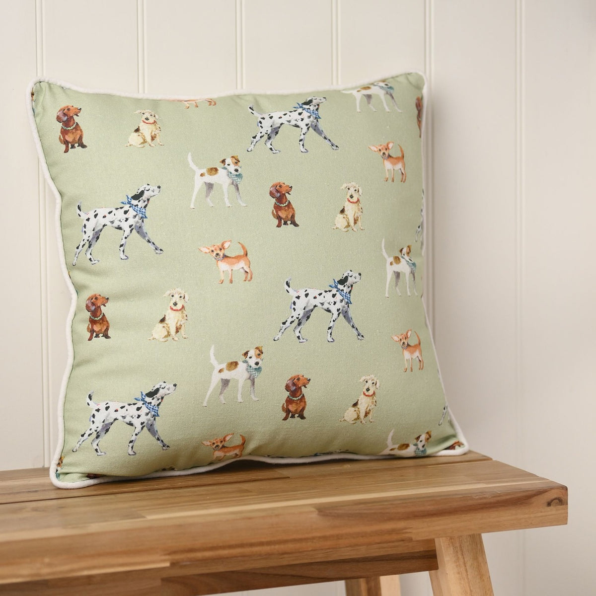 Square cushion, 42cm x 42cm, in lime green with a scattered dog print and cream piped edge, shown on a wooden bench against a panelled wall.