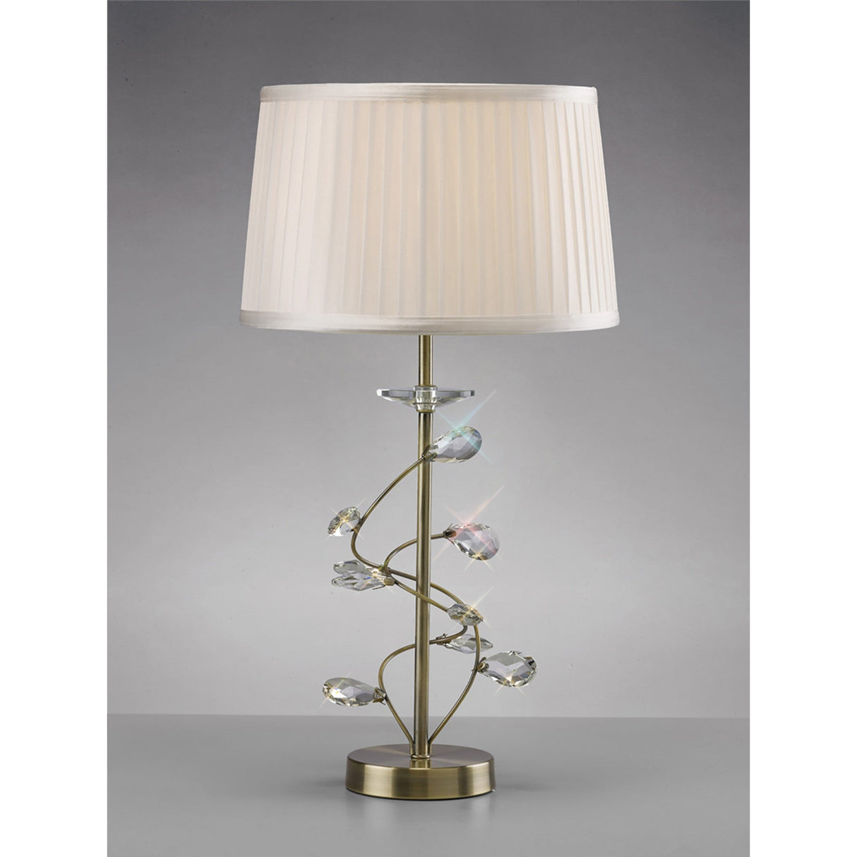 The Willow 1 Light Crystal Table Lamp features an antique brass finish, a spiral stem with crystal accents, and a pleated white shade on a gold metal base. Set against a plain gray background.