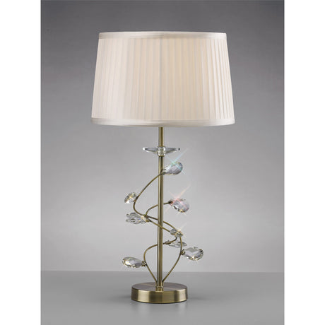 The Willow 1 Light Crystal Table Lamp features an antique brass finish, a spiral stem with crystal accents, and a pleated white shade on a gold metal base. Set against a plain gray background.