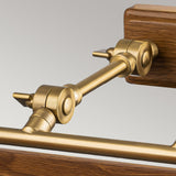 A close-up of the Winchfield 4 Light Large Picture Light in aged brass and oak effect, featuring lever arms against a wooden and metal framework. The polished mechanical joint connects horizontal and vertical rods, highlighting the intricate design and engineering details.
