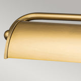 The Winchfield 4 Light Large Picture Light in aged brass features a sleek cylindrical shade and a curved top design, exuding Mid Century Modern elegance. Its modern aesthetic beautifully contrasts against a neutral gray background to add a touch of sophistication.