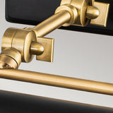 A close-up of the Winchfield 2 Light Medium Picture Light in aged brass and matte black showcases its modern wall-mounted design with adjustable joints and a sleek, rectangular silhouette. The image emphasizes the lamp's polished metal finish and elegant construction against a neutral background, making it an ideal sophisticated picture light for your space.
