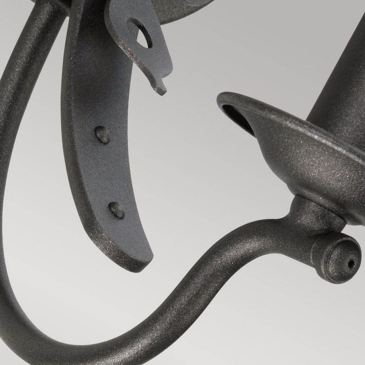 Close-up of a dark metal bracket or hook with a graphite finish against a plain gray background. The image highlights the Windsor 1 Light Wall Light - Graphite, showcasing its elegantly curved and textured surfaces, with visible bolts for attachment, drawing inspiration from British heritage.