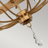 Close-up of the exquisite Windsor 12 Light Chandelier - Gold Patina, showcasing its clear crystal pendants elegantly suspended from curved metal arms. The plain light gray background accentuates the chandelier's British craftsmanship.