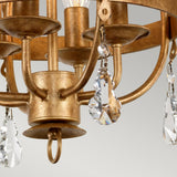 Close-up of the Windsor 4 Light Chandelier - Gold Patina, featuring a stunning finish with clear crystal pendants. It showcases intricate curved arms and ornate design details, epitomizing timeless elegance.
