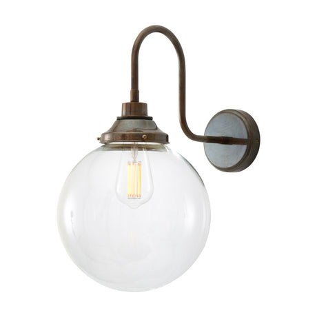 Wistella swan neck wall light with brass arm and round wall plate, holding a clear 25cm glass globe shade with visible E27 bulb, shown on a white background.