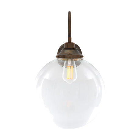 Wistella Glass Swan Neck Globe Wall Light, 30cm clear glass globe shade on an aged brass swan neck arm with round wall plate, visible bulb, shown on a plain white background.