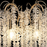 Close-up of the Wisteria 4 Light Crystal Floor Lamp in French Gold, featuring clusters of clear crystals and two glowing bulbs on a reflective metal frame, elegantly set against a black background.