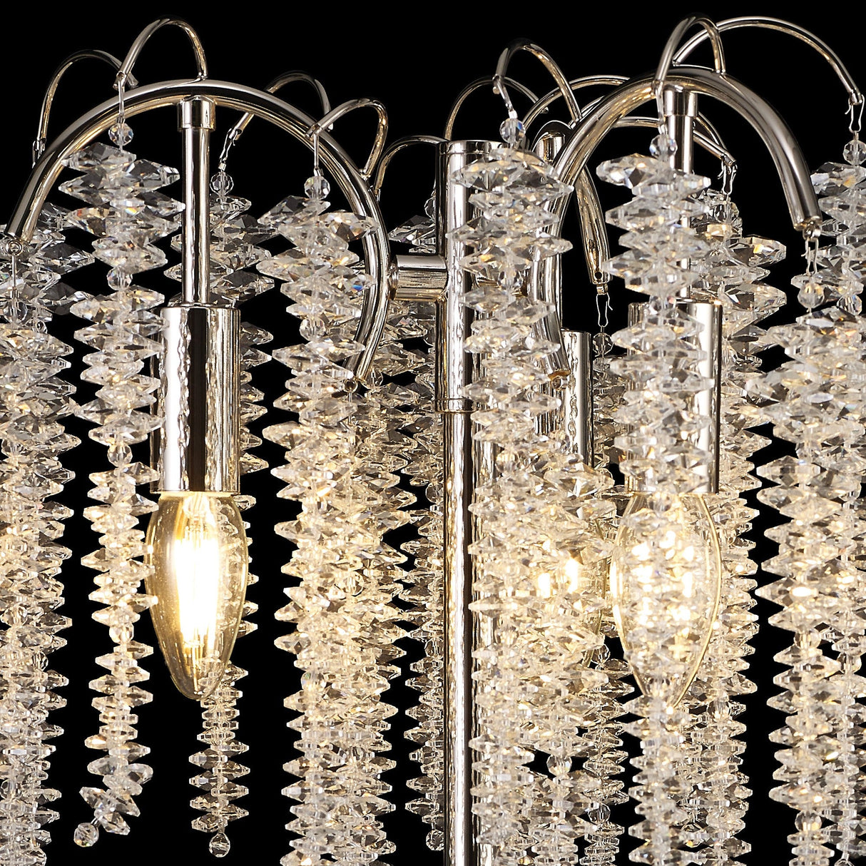 Close-up of the Wisteria 3 Light Table Lamp, featuring nickel finish and clear crystal clusters on curved arms with three exposed bulbs, creating elegant ambient lighting against a black background.